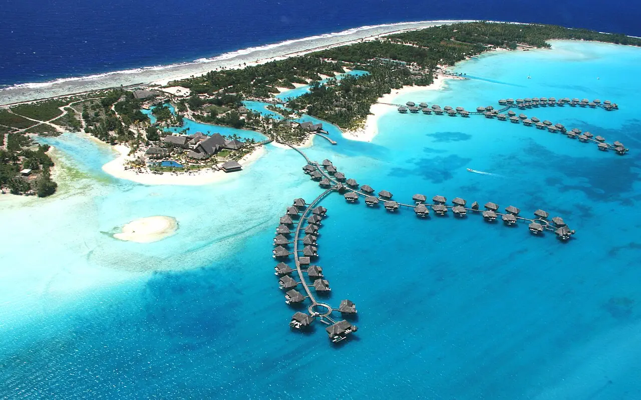 Aerial view of overwater bungalows curving across a turquoise lagoon in Bora Bora