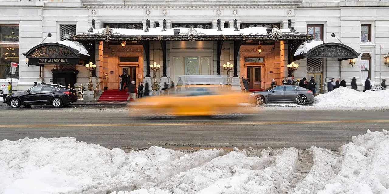 Entrance of The Plaza hotel in winter snow with a yellow taxi passing